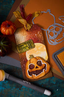 Halloween-themed cookie with pumpkin design and candy on a rustic surface.