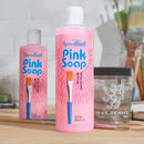 Two bottles of Speedball Pink Soap on a table with art supplies in the background.