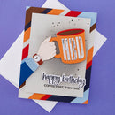 Birthday card with a hand holding a mug labeled 'HIS' and text 'happy birthday, coffee first, then cake' on a colorful striped border.