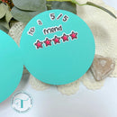 Teal circular stamp with text and star ratings on a white doily with greenery