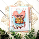 Card with cartoon characters and heart design on a decorative surface with plants.