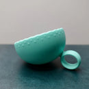 Teal silicone teether on a dark surface with a light gray background