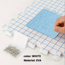 White EVA foam tile with blue textured patch on a grid surface, with pins and a container of pins.