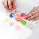 Colorful stamp with a hand holding it over a sheet of paper with printed designs.
