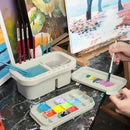 Artistic setup with paintbrushes, watercolor paints, and a palette on a table.