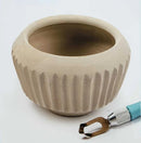Beige ceramic bowl with textured surface on a white background, accompanied by a ceramic tool.