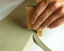 Hand using a wooden tool to cut fabric on a white background