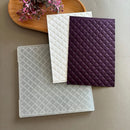Four textured notebooks in white, purple, and clear on a neutral background