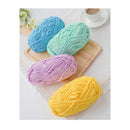 Four balls of yarn in blue, green, purple, and yellow on a wooden board with a cup of coffee in the background.