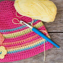 Crocheted multicolored fabric with a ball of yellow yarn and a blue crochet hook on a wooden surface.
