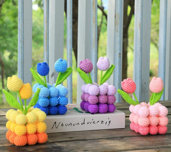 Colorful crocheted tulip sculptures on a wooden surface with a blurred natural background.