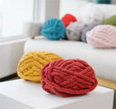 Colorful knitted pillows on a white surface with a blurred sofa in the background