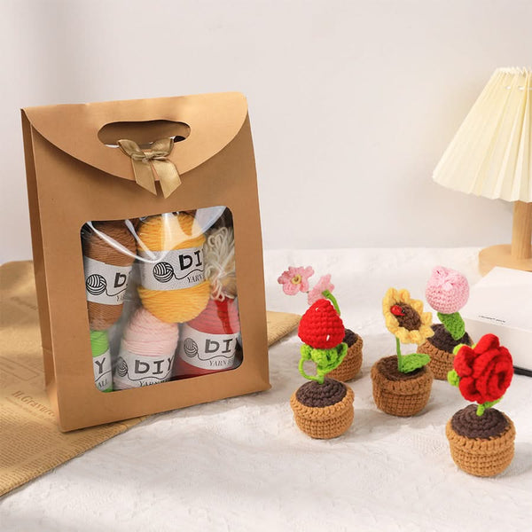 Crocheted flower pots with yarn balls in a packaging box on a light background