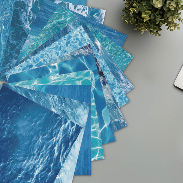 Stack of blue water-patterned paper sheets on a gray surface with a plant in the corner.