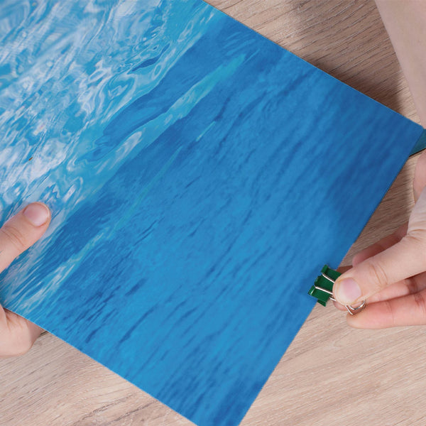 Person holding a blue textured paper with a green clip on a wooden surface