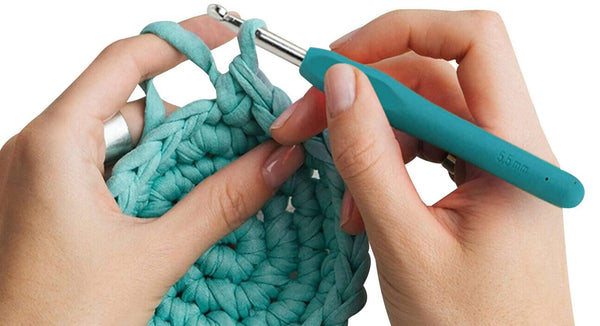 Teal crochet hook being used to work on a teal crocheted item with a white background