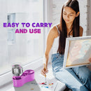Woman sitting by a window with art supplies, including a purple container and paint palette.
