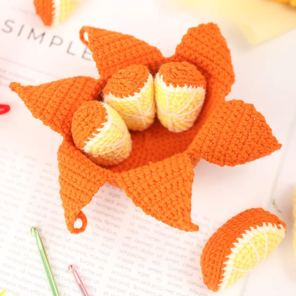 Crocheted orange and yellow flower with a crochet hook on a white background