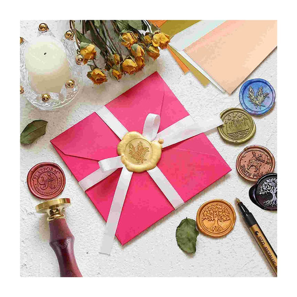 Pink envelope with a gold wax seal surrounded by various seals and a candle on a textured surface.