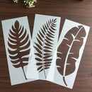 Three leaf-shaped stencils on a wooden surface with small flowers in the background.