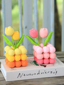 Two crocheted tulip bouquets, one yellow and one pink, on a book with blurred background.