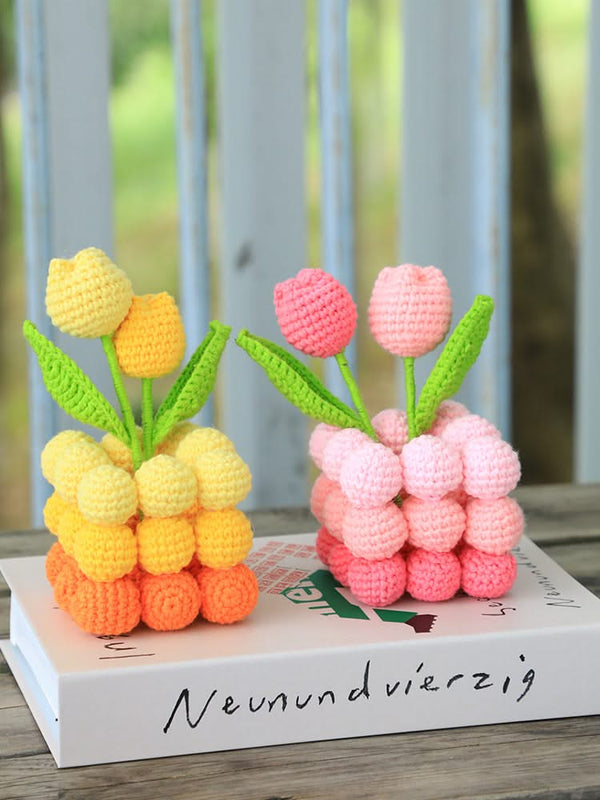 Two crocheted tulip bouquets, one yellow and one pink, on a book with blurred background.