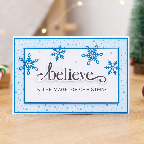 Christmas card with blue snowflakes and 'believe in the magic of Christmas' text on a light background.