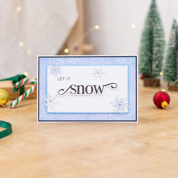 Christmas card with 'Let It Snow' text on a festive background with decorations.