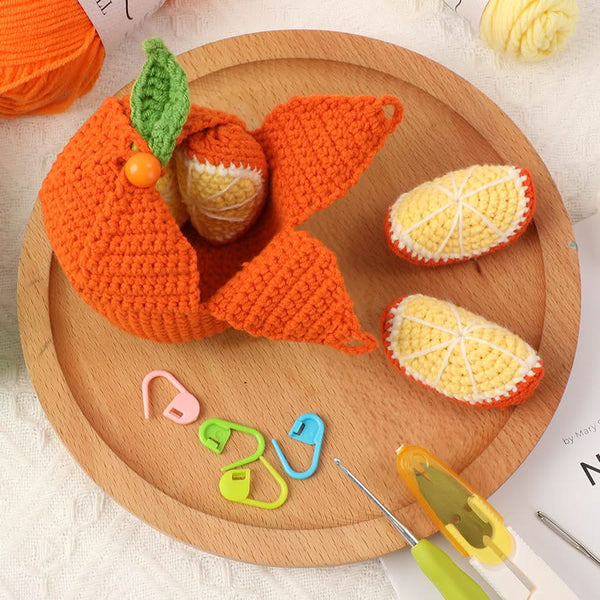 Knitted orange fish and lemon slices on a wooden plate with crochet tools.