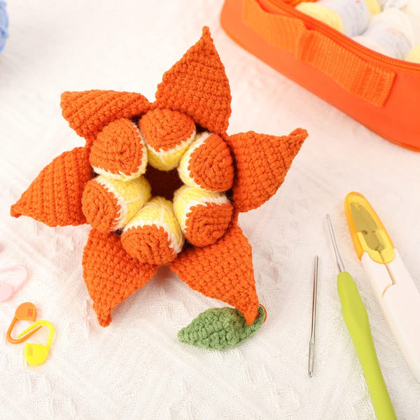 Crocheted orange flower with yellow centers on a white surface, with crochet tools nearby.