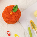 Crocheted orange with a green leaf on a beige surface with crochet tools.