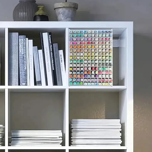 White bookshelf with books, a box of watercolor paints, and stacks of papers.