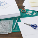 Crafting materials including paper, scissors, and stencils on a cutting mat.