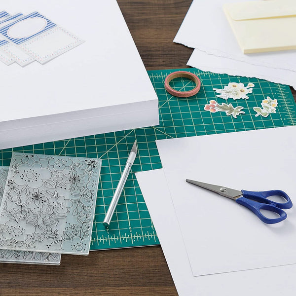 Crafting materials including paper, scissors, and stencils on a cutting mat.