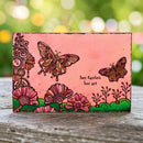 Decorative wooden block with butterfly and floral designs on a pink background, placed outdoors.