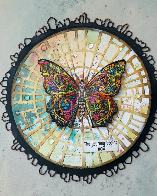 Decorative circular piece with a colorful butterfly and 'The Journey Begins Now' text on a textured surface.