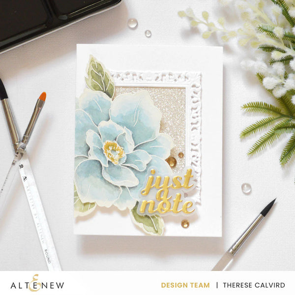 Card with floral design and 'just a note' text on a white surface with stationery items.