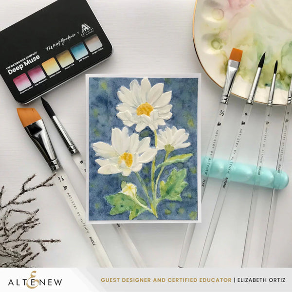 Artistic watercolor painting of daisies with painting tools and Altenew product on a white surface.
