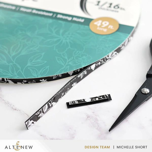 Scissors with black and white patterned handles on a white surface with a green cutting mat in the background.