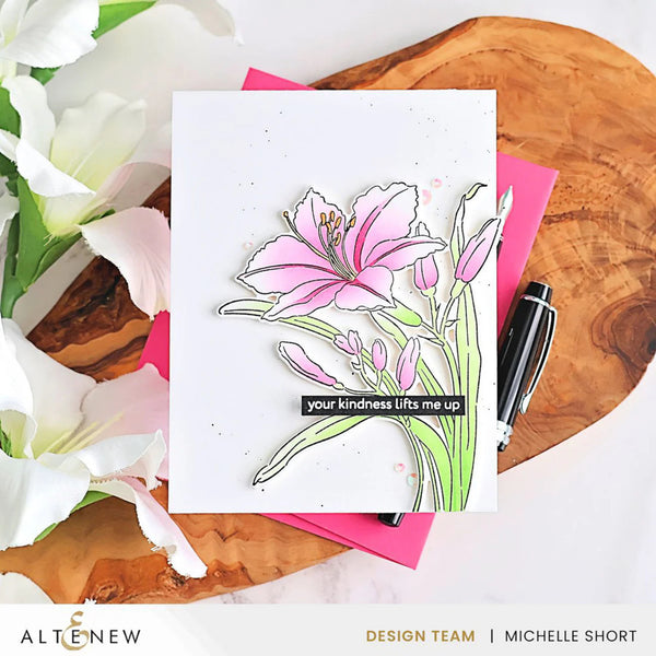 Card with floral design and message on a wooden surface with flowers and a pen.
