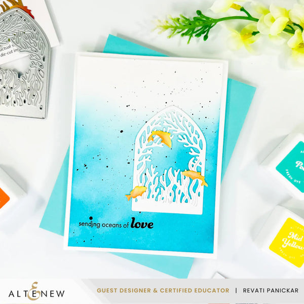 Card with ocean-themed design and 'sending oceans of love' text, surrounded by crafting tools and flowers on a white background.
