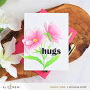 Card with pink flowers and 'hugs' text on a wooden surface with flowers.