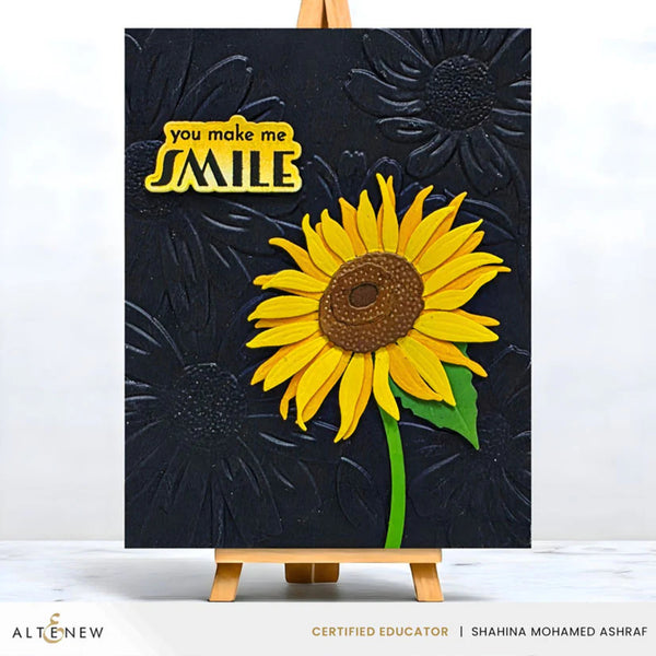 Artistic depiction of a sunflower with 'you make me smile' text on a black background, displayed on an easel.