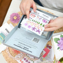 Hands opening a box of floral stickers with a QR code on a table.