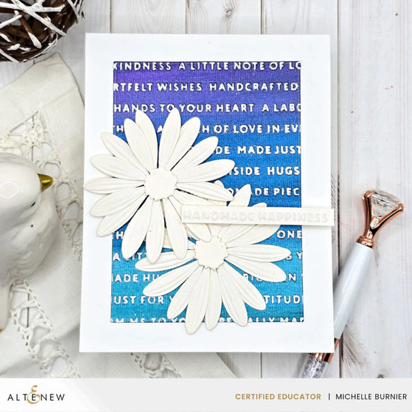 Card with white flowers on a blue background with text, placed on a wooden surface.