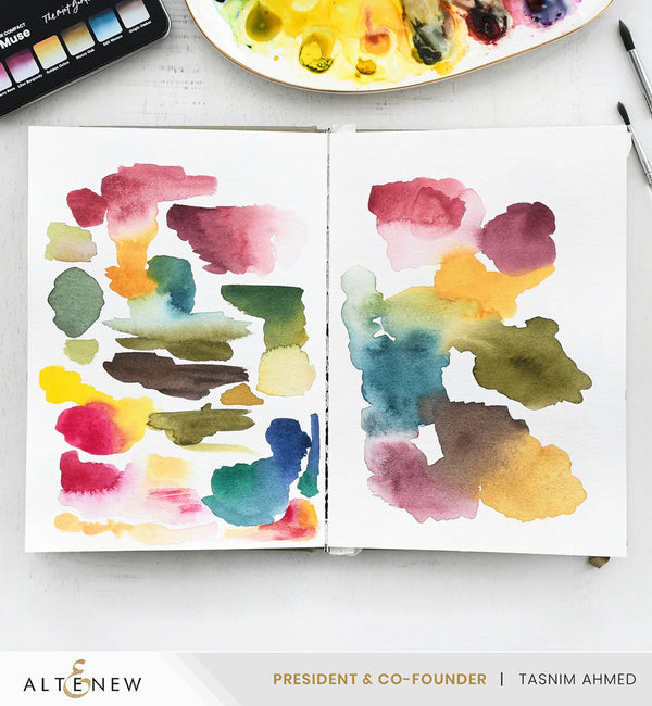 Open book with watercolor swatches on a white surface, with 'Altenew' branding visible.
