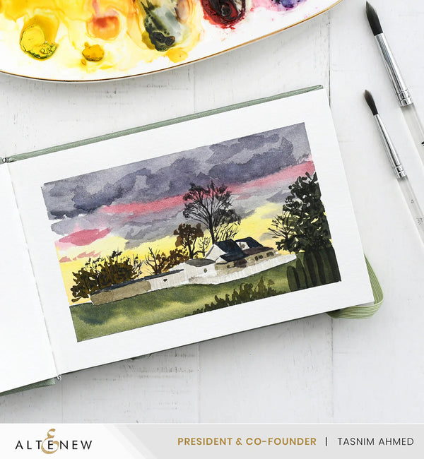 Watercolor painting of a landscape with trees and a house, displayed on a white surface with art supplies.