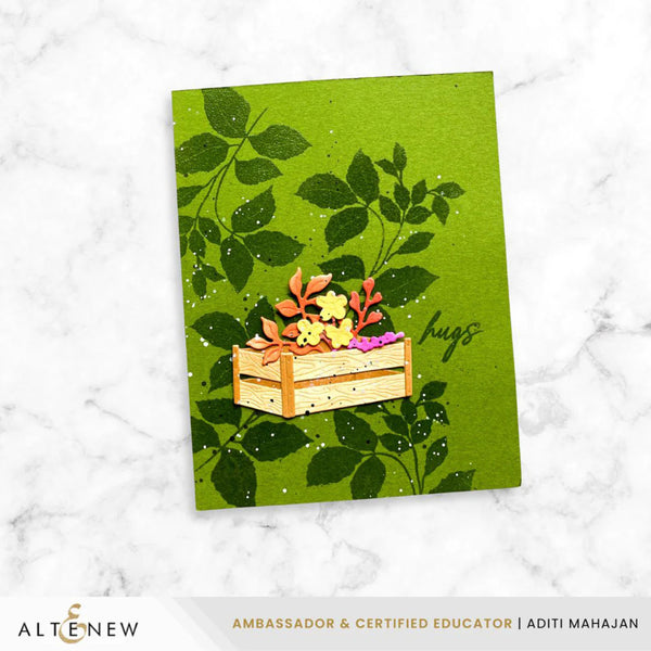 Card with a wooden crate of flowers and leaves on a green background, featuring the brand 'Altenew'.