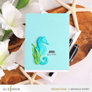 Card with a seahorse design and 'sea you later' text on a wooden surface with flowers and stationery.