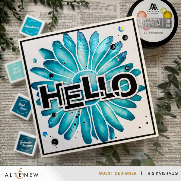 Card with blue floral design and 'HELLO' text, surrounded by craft supplies on a textured surface.